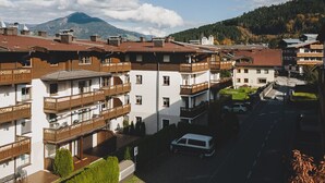 A multi-story building with balconies, a parking area, and a mountain in the background. - Ski & Golf Suite 25: balcony, Maiskogel View (Kaprun)