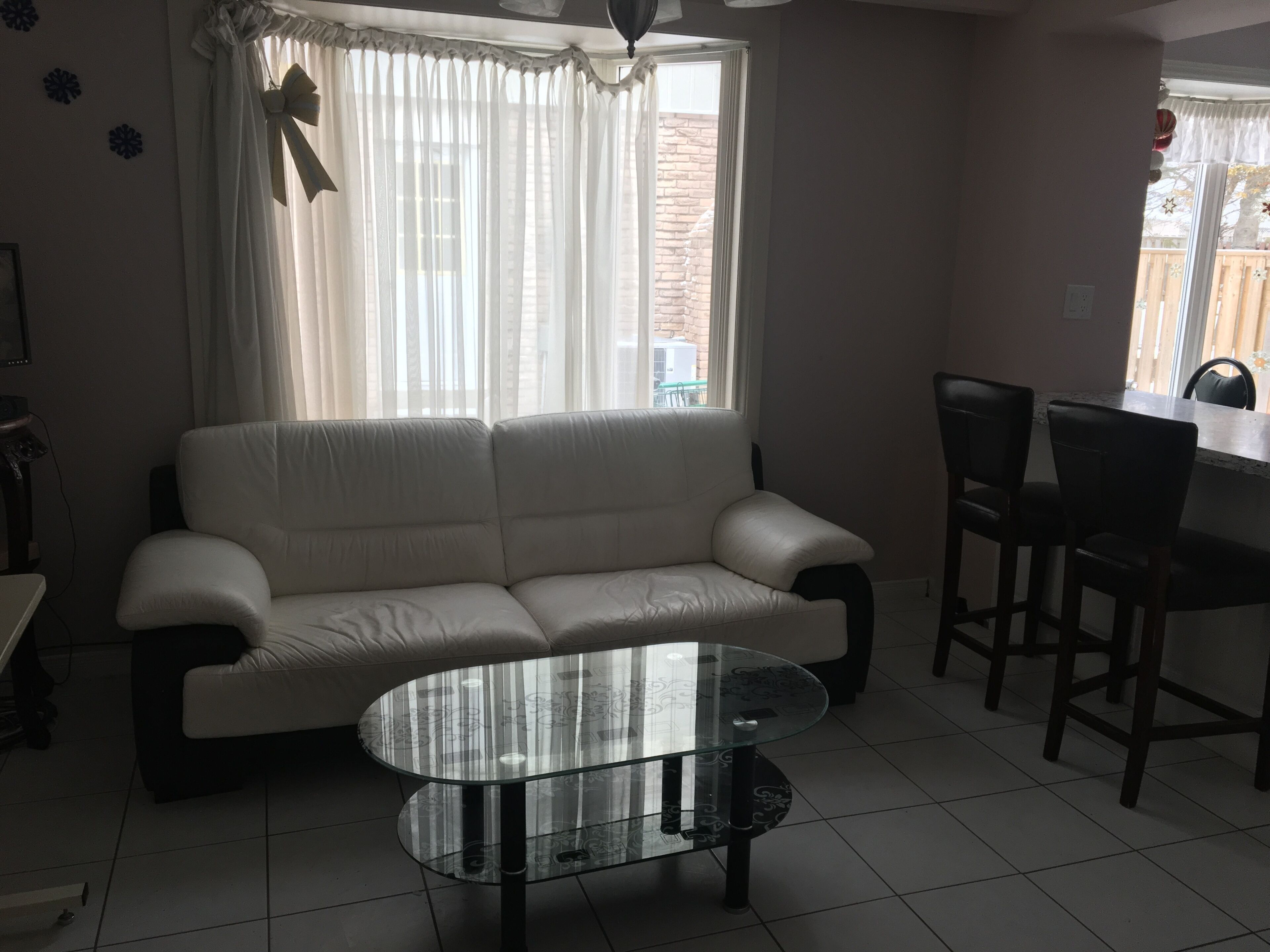 Een woonkamer met een witte bank, een glazen salontafel en een eethoek met stoelen.