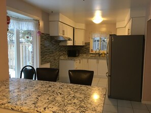A kitchen with a granite countertop, white cabinets, a stainless steel refrigerator, and a window with a view of the outside. - Clean and Quit (Toronto)