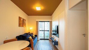 A compact hotel room with a sofa, a dining table, a TV, and a large window. - Studio with Parking Space in the Heart of Itaim (São Paulo)