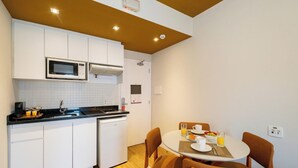 A compact kitchen with white cabinets, a microwave, and a sink. There is a dining table with chairs and a breakfast setting. - Studio with Parking Space in the Heart of Itaim (São Paulo)