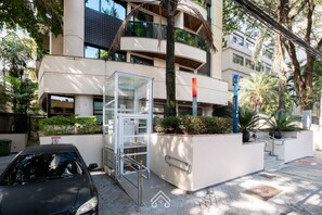 A modern building with a glass elevator, a car parked in front, and a staircase leading to the entrance. - Cozy Studio Itaim Bibi (São Paulo)