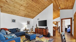 Un salon avec un plafond en bois, un canapé, un téléviseur et un tapis à motifs.