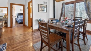 Une table à manger en bois avec des chaises, une cheminée, un lit et une fenêtre avec des rideaux.
