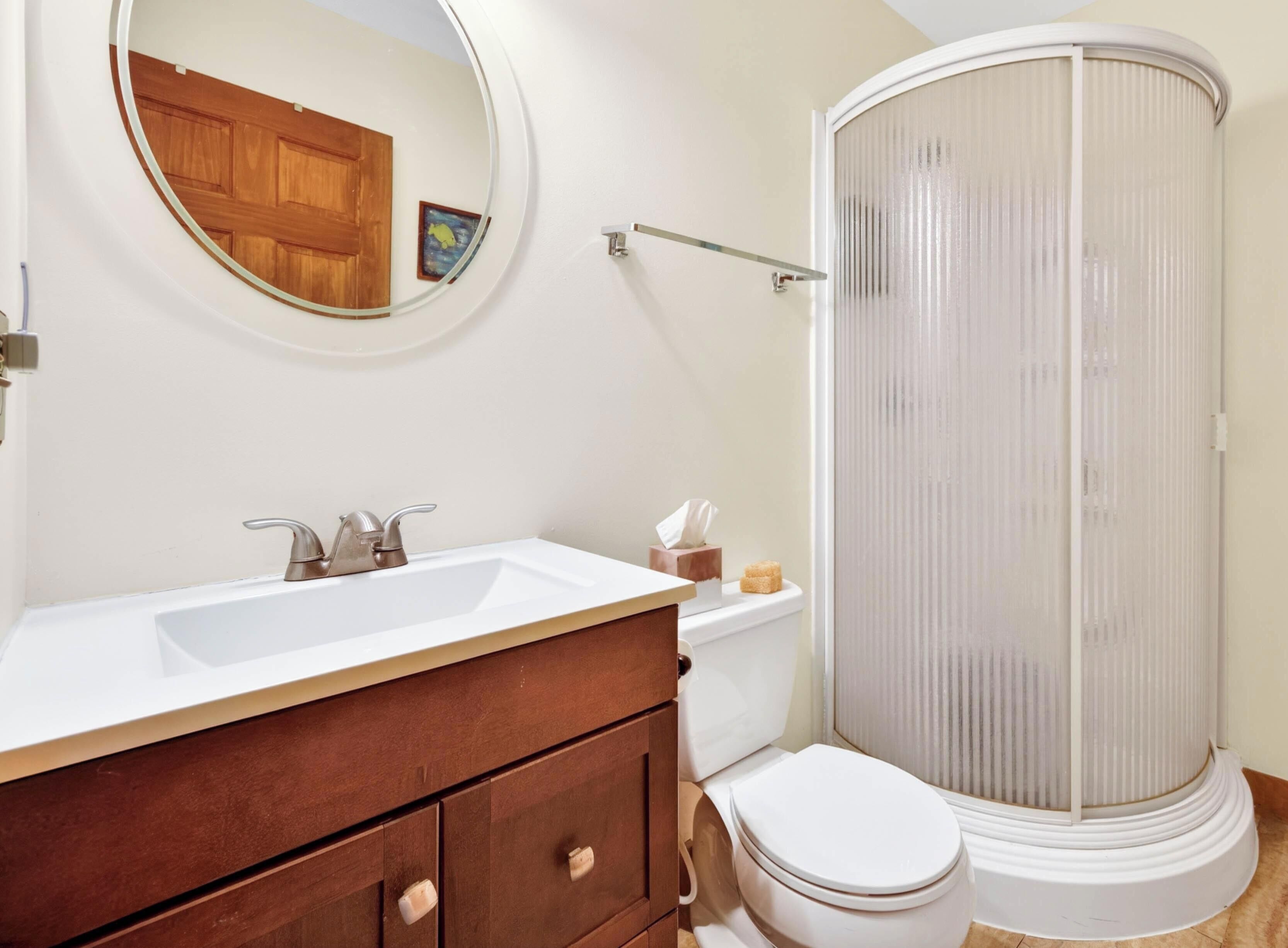 A bathroom with a white sink, a mirror, a toilet, and a shower enclosure.