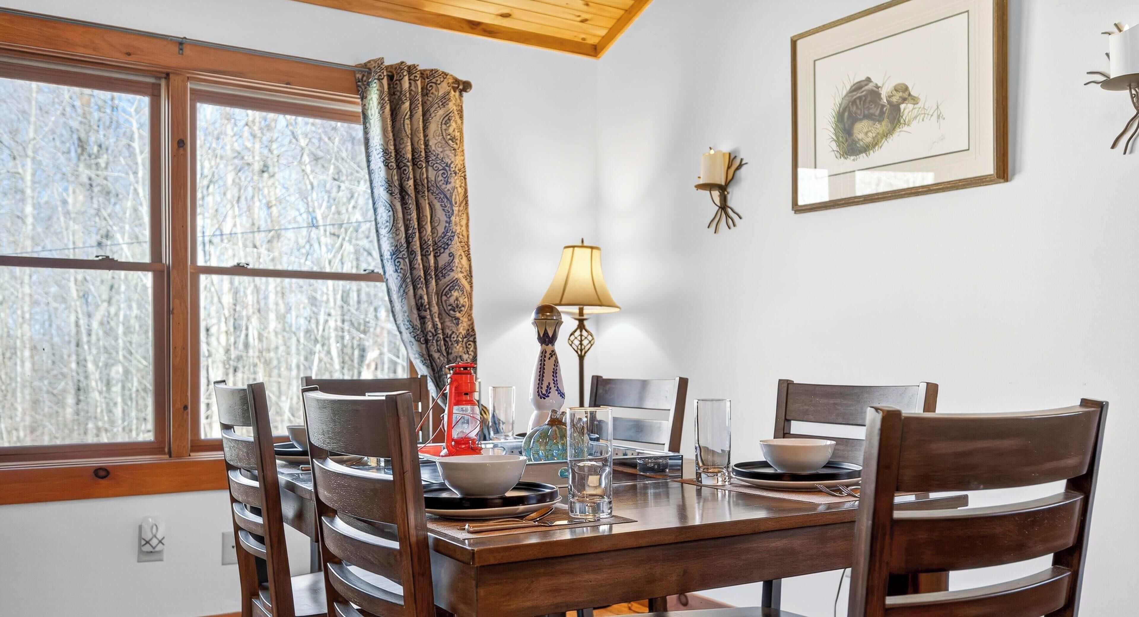 A dining area with a wooden table, chairs, a candle, a lamp, and a framed picture on the wall.