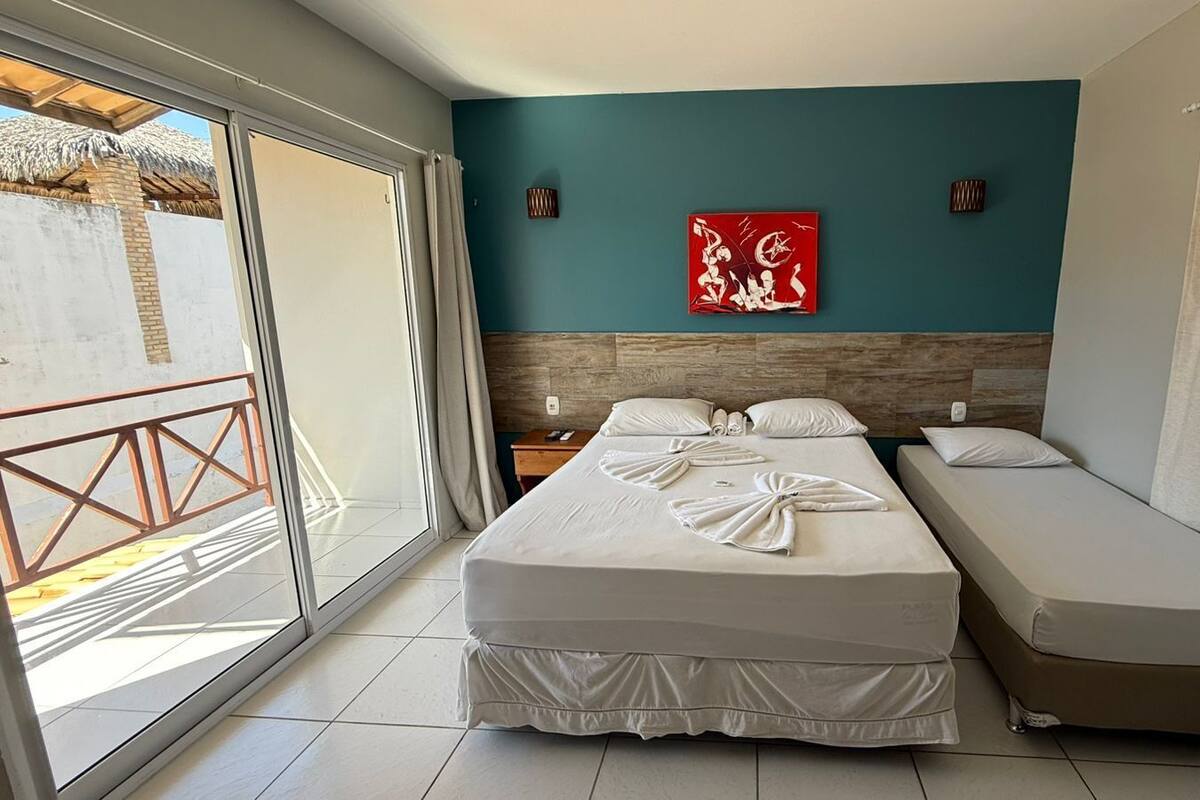 A hotel room with a bed, a sofa, a large window, and a red artwork on the wall.