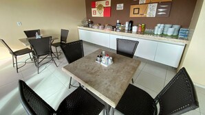 Un comedor con mesa y sillas, una encimera de cocina con diversos objetos, y una pared decorada con obras de arte.