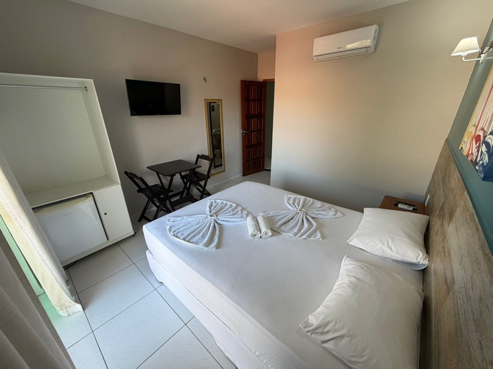 Habitación de hotel con cama, escritorio, silla, televisor y aire acondicionado.