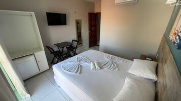 Habitación de hotel con cama, escritorio, silla, televisor y aire acondicionado.