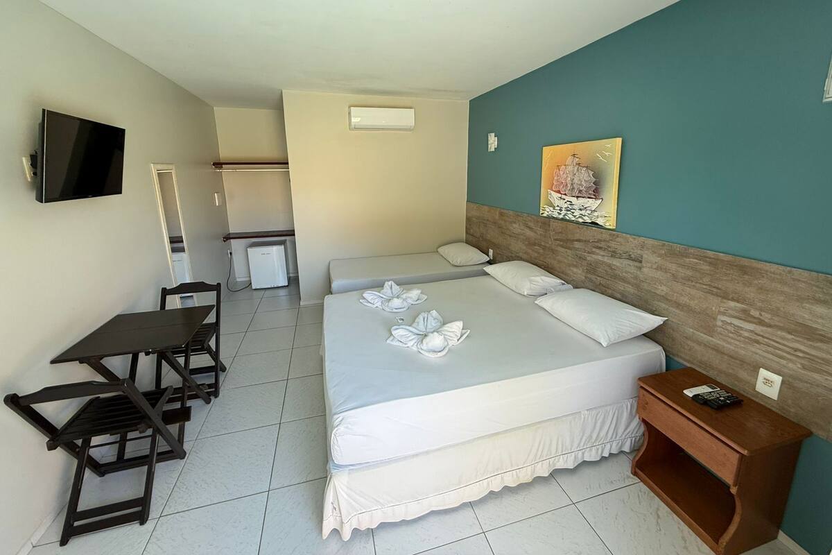 A hotel room with a bed, a desk, a chair, a TV, and a small refrigerator.