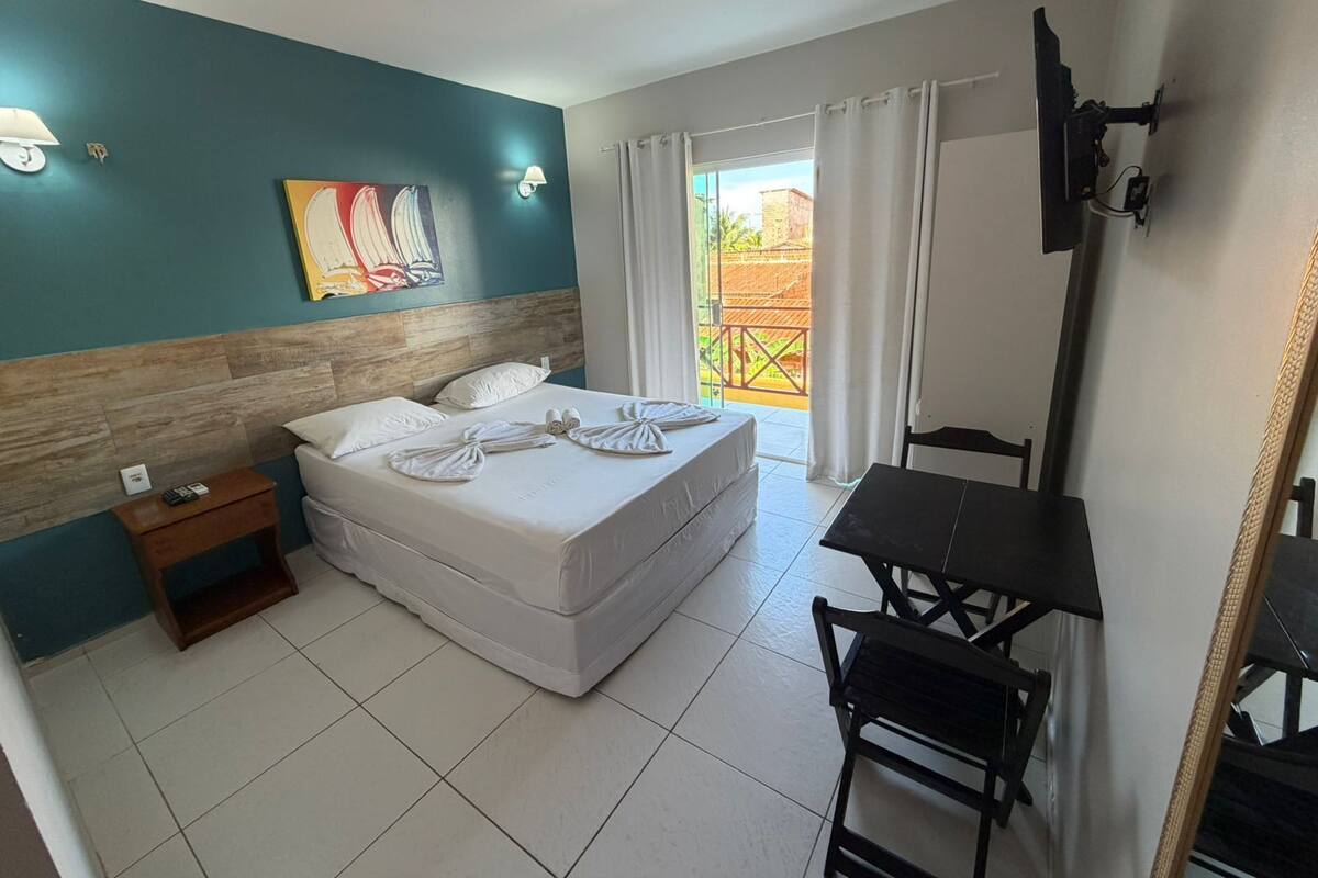 A hotel room with a bed, a desk, a chair, a small table, and a painting on the wall.