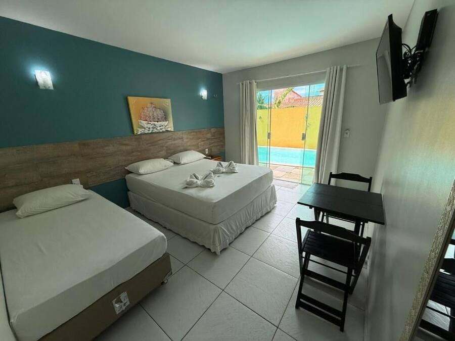 Habitación de hotel con dos camas, una mesa de comedor y vista a una piscina.