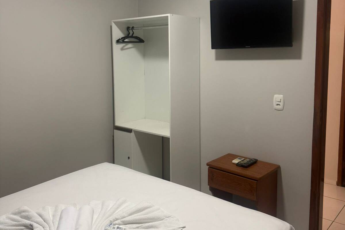 A hotel room with a bed, a TV, a wardrobe, and a small bedside table.