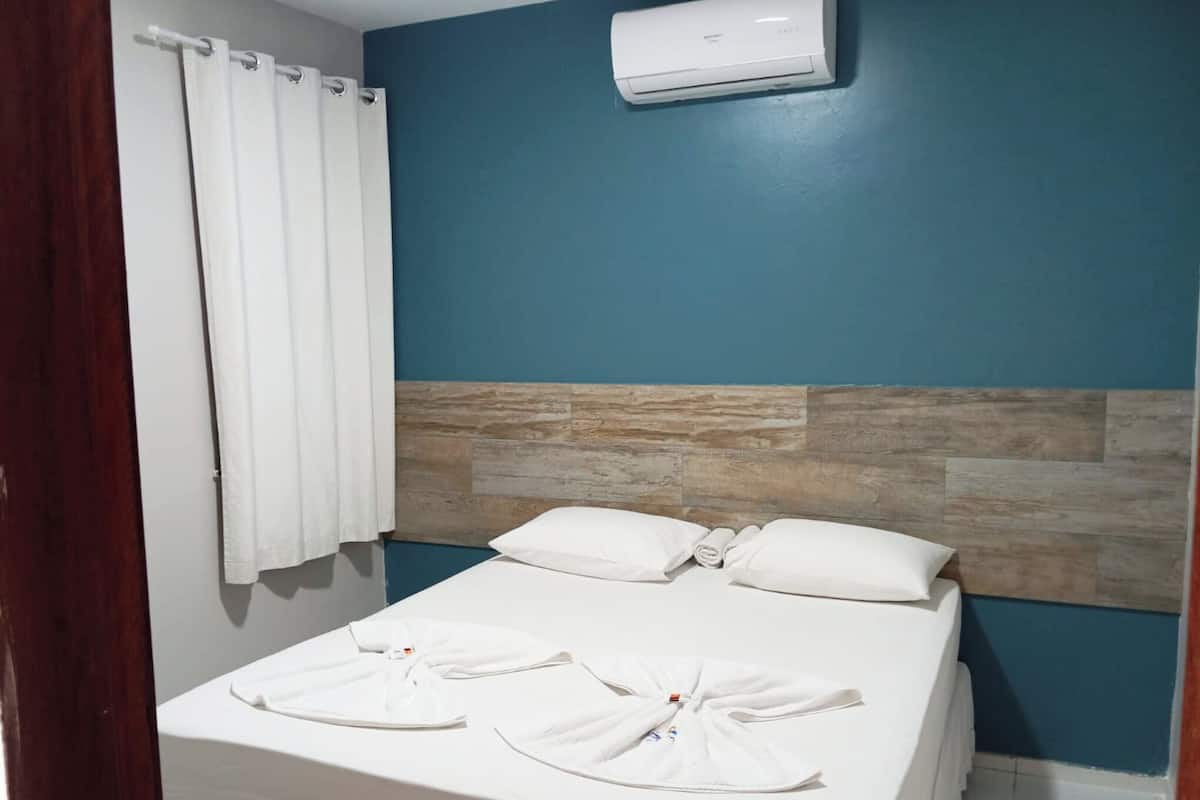 A hotel room with a bed, white towels, a curtain, and an air conditioning unit.