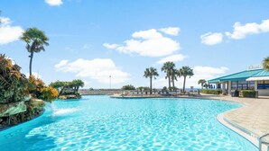Une piscine d’un bleu éclatant, avec un poste de surveillance pour les sauveteurs, des palmiers et un bâtiment portant l’inscription « Ocean’s ».