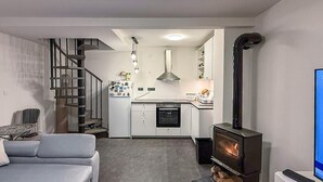 Eine moderne Küche mit Einbauofen, Essbereich mit Tisch und Stühlen, eine Treppe und ein Kaminofen.