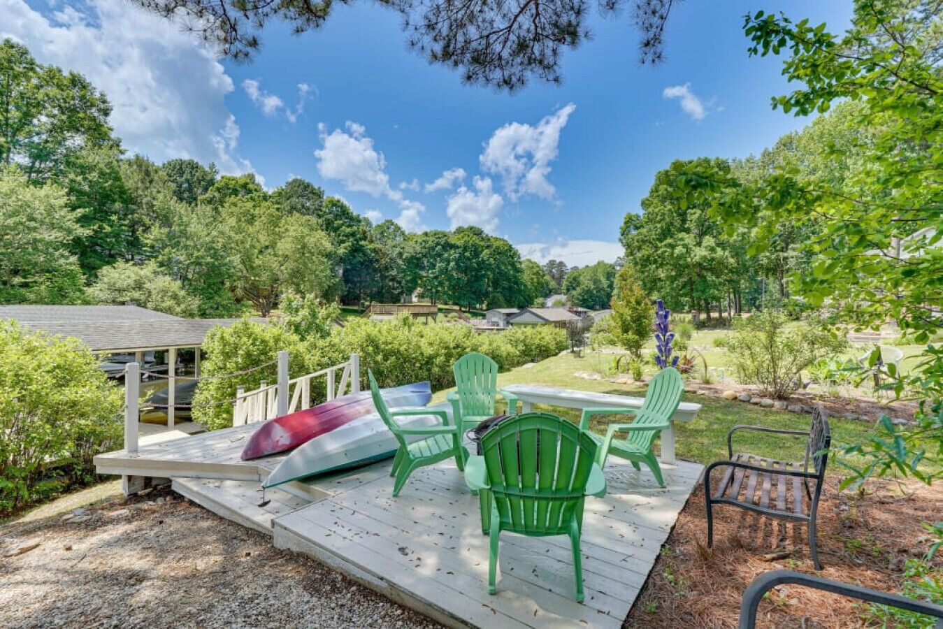 A deck with chairs and a canoe, surrounded by greenery and a clear sky.