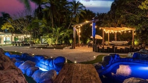 Ein Außenbereich bei Nacht mit einer Holzterrasse, einem Whirlpool und einem Pavillon mit Lichterketten.