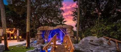 A naturalistic outdoor area with a wooden bridge, a water feature, and a rock formation.
