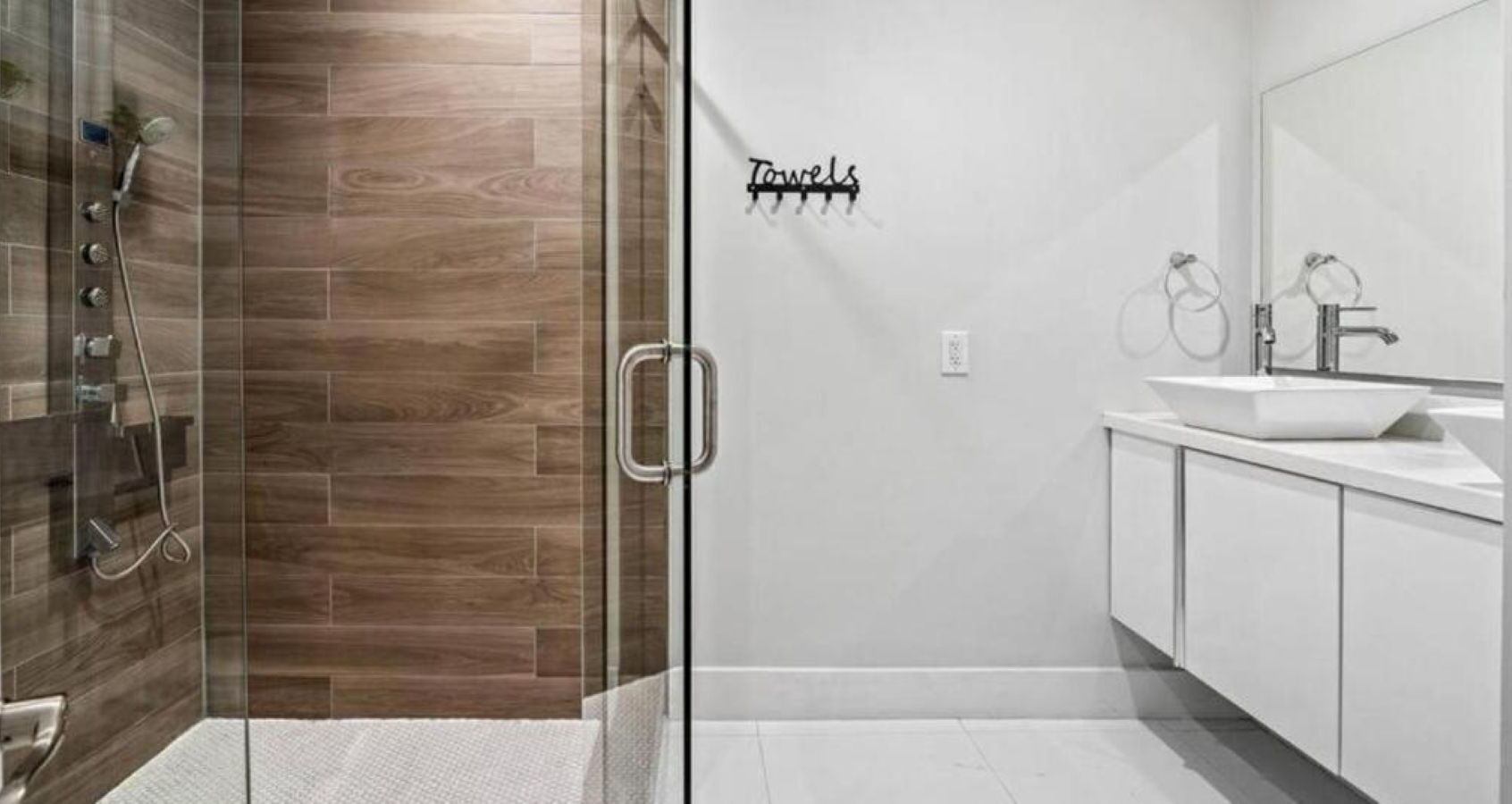 Un baño moderno con cabina de ducha de vidrio, un lavabo blanco y un perchero para toallas.