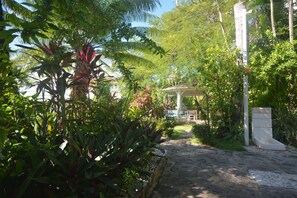A stone pathway leading to a covered area surrounded by lush greenery and a white structure. - 2-bedroom apartment practically facing the sea (Las Terrenas)