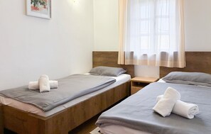 A double room with two beds, each with a wooden headboard, a small bedside table, and a window with sheer curtains.