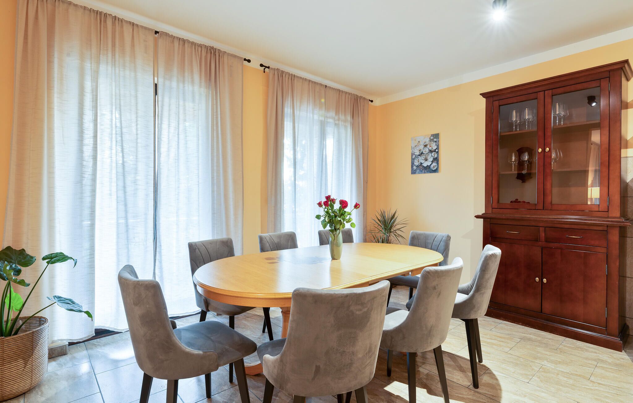 Ein Essbereich mit einem runden Tisch, sechs Stühlen, einer Blumenvase und einem Schrank mit Glastüren.
