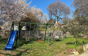 A playground with a blue slide, swings, and a stone wall in the background. - Cozy home in Donji Humac (Donji Humac)