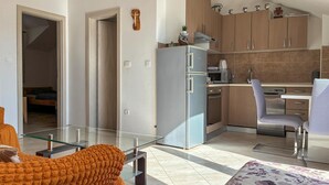 A modern kitchen with a refrigerator, microwave, and stove, a glass dining table, and a sofa with a blanket. - 2 bedroom gorgeous apartment in Donji Humac (Donji Humac)