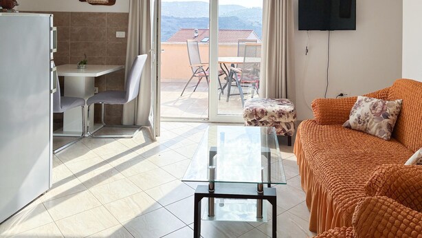 A living room with a sofa, a glass coffee table, a TV mounted on the wall, and a balcony with a table and chairs. - 2 bedroom gorgeous apartment in Donji Humac (Donji Humac)