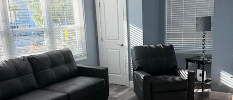A living room with a black leather sofa, a black armchair, a round rug, and a lamp on a side table.