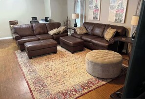 A living room with a brown leather sectional sofa, two ottomans, a patterned rug, and a round ottoman. - Oasis in the Narragansett Pier. Family retreat home Comfortably sleeps 12 (Narragansett)