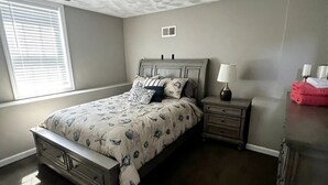 Un dormitorio con cama, mesitas de noche, lámpara y ventana con persianas.