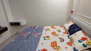 A bedroom with a bed, pillows, a bedside table, and a wall-mounted shelf.