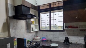 A kitchen with a gas stove, a black range hood, a window with bars, and a refrigerator.