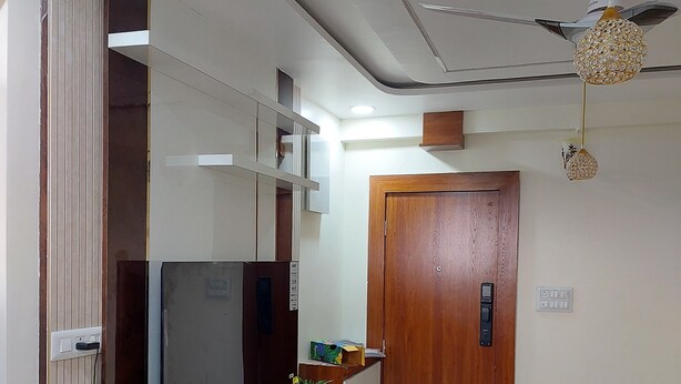 A hallway with a ceiling fan, a wooden door, and a wall-mounted light fixture.