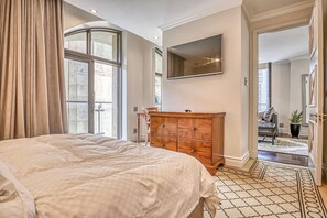 Ein Schlafzimmer mit einem großen Bett, einer hölzernen Kommode, einem Flachbildfernseher und Blick ins Freie.