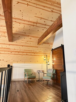 Eine Holzbalkendecke, Holzboden und zwei grüne Sessel mit einem kleinen Tisch und einer Lampe.