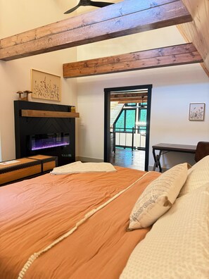 Ein Schlafzimmer mit Bett, Kamin, Holzboden und Blick ins Freie.