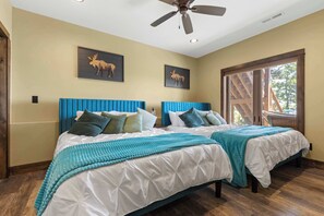 A bedroom with two beds, a ceiling fan, and two framed animal pictures on the wall.