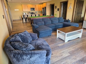 A living room with a sectional sofa, a coffee table, and a pool table.