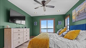 A bedroom with a bed, a dresser, a ceiling fan, a TV, and a window with a view of a body of water. - Lake Front | Pontoon | Private Beach | Hot Tub (New Lisbon)