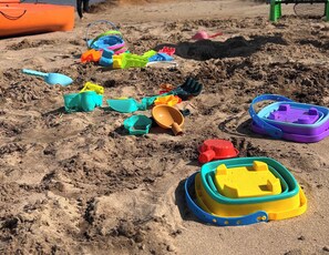 Ein sandiger Bereich mit verschiedenen bunten Sandspielzeugen und einer kleinen blauen Schaufel.