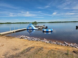 A calm lake with a dock, a blue inflatable structure, and a blue and white inflatable ring.