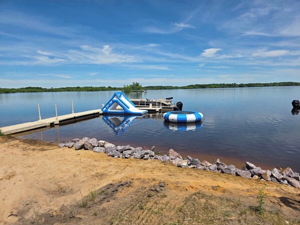Ein ruhiger See mit einer Anlegestelle, einer blauen aufblasbaren Struktur und einem blau-weißen Schwimmreifen.