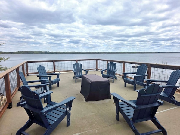 A deck with Adirondack chairs and a table, overlooking a body of water.