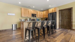 A kitchen with wooden cabinets, a stainless steel refrigerator, a sink, and bar stools. - Lake Front | Pontoon | Private Beach | Hot Tub (New Lisbon)
