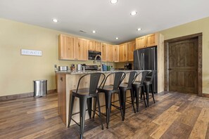 A kitchen with wooden cabinets, a stainless steel refrigerator, a sink, and bar stools.