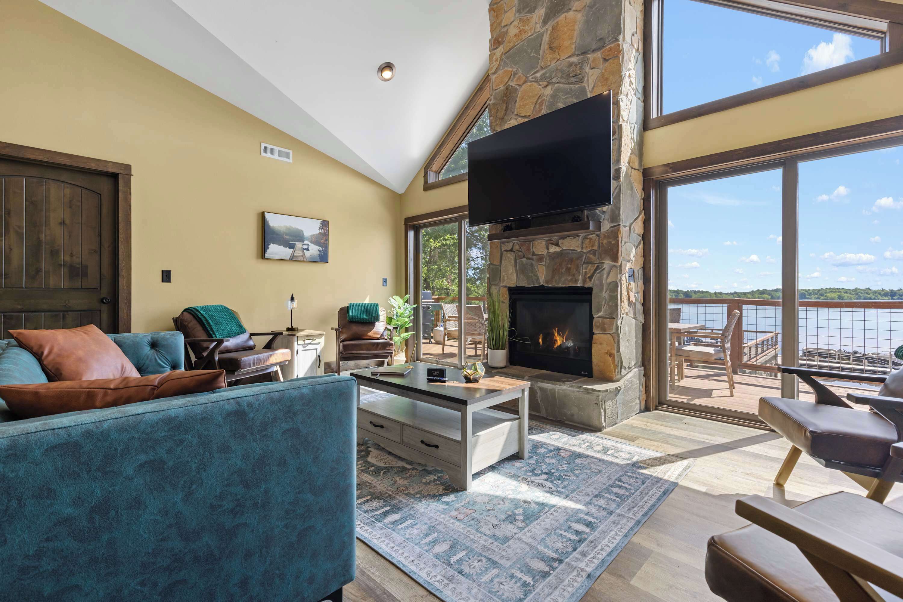 Amplia sala de estar con chimenea de piedra, un televisor de pantalla plana grande y vistas al exterior.